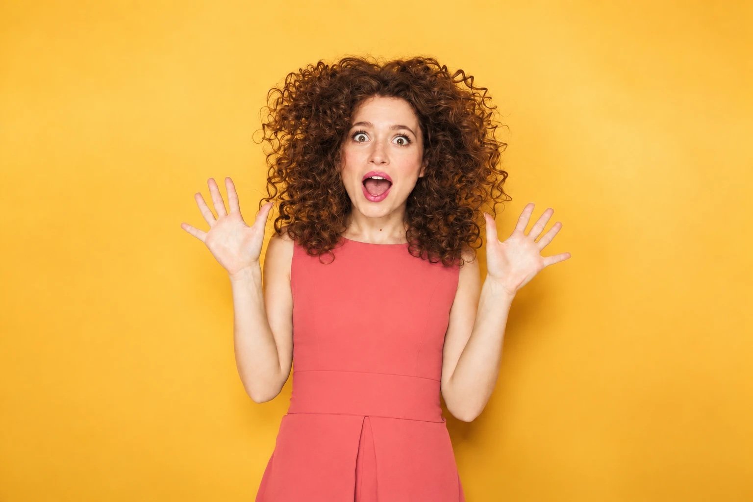 Amazed, happy woman with her hands up on a yellow background